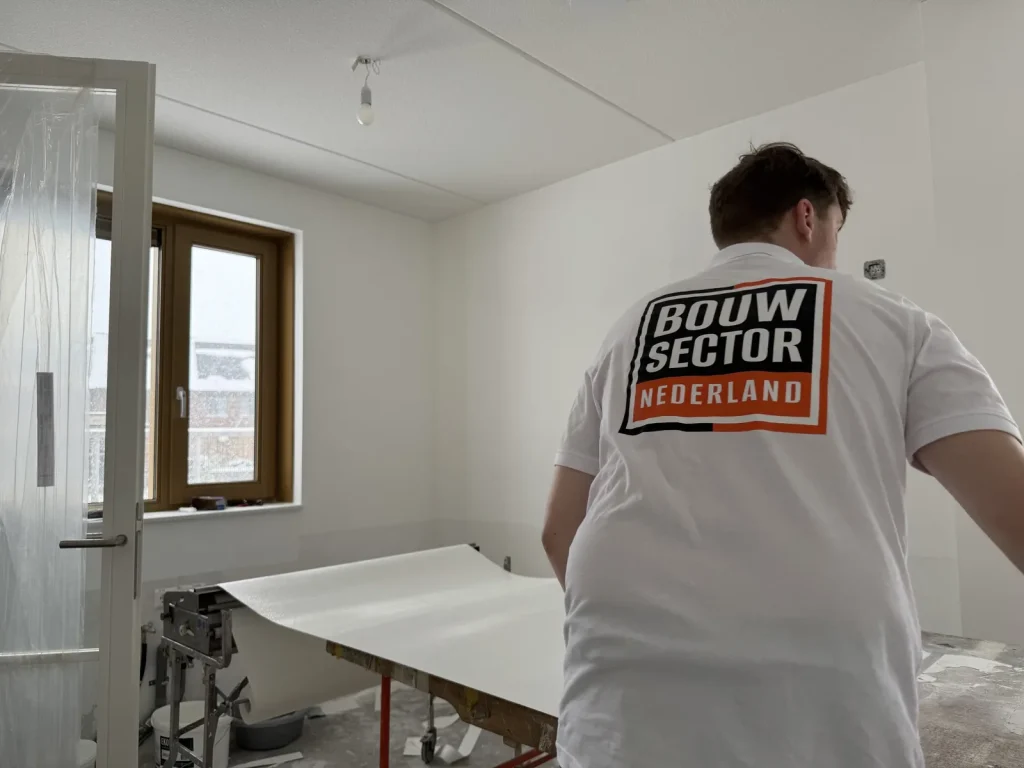 Behanger in wit werkshirt van Bouwsector Nederland met een baan behang op de plaktafel
