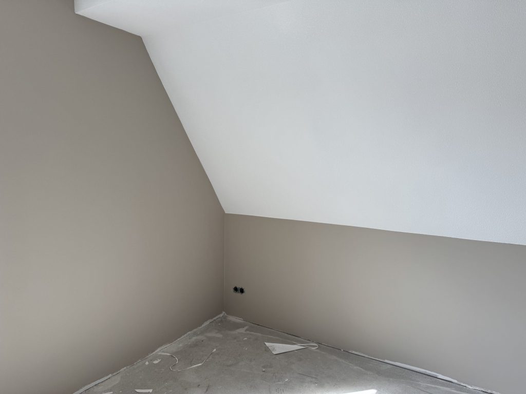 Kamer met een schuine wand onder het dak, de muren in een zachte zandtint afgewerkt