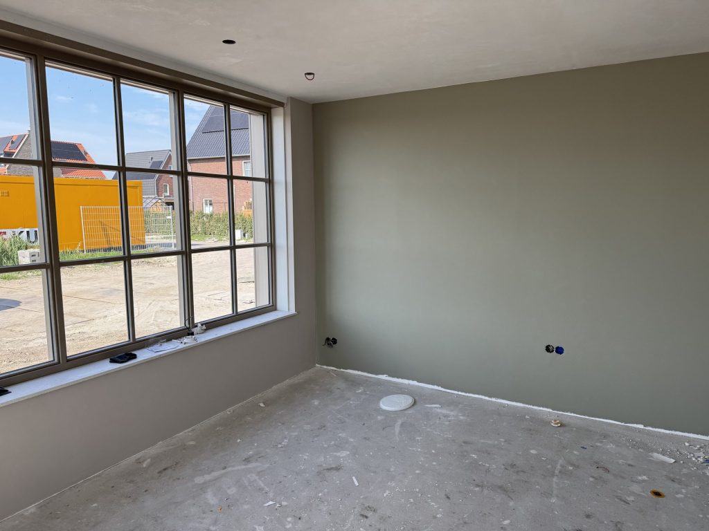 Kamer met een groot raam en een wand in een grijsgroene tint als blikvanger