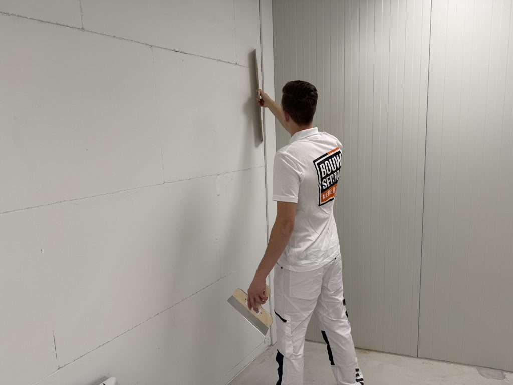 Stukadoor van Bouwsector Nederland trekt een muur vlak voordat er behang op komt