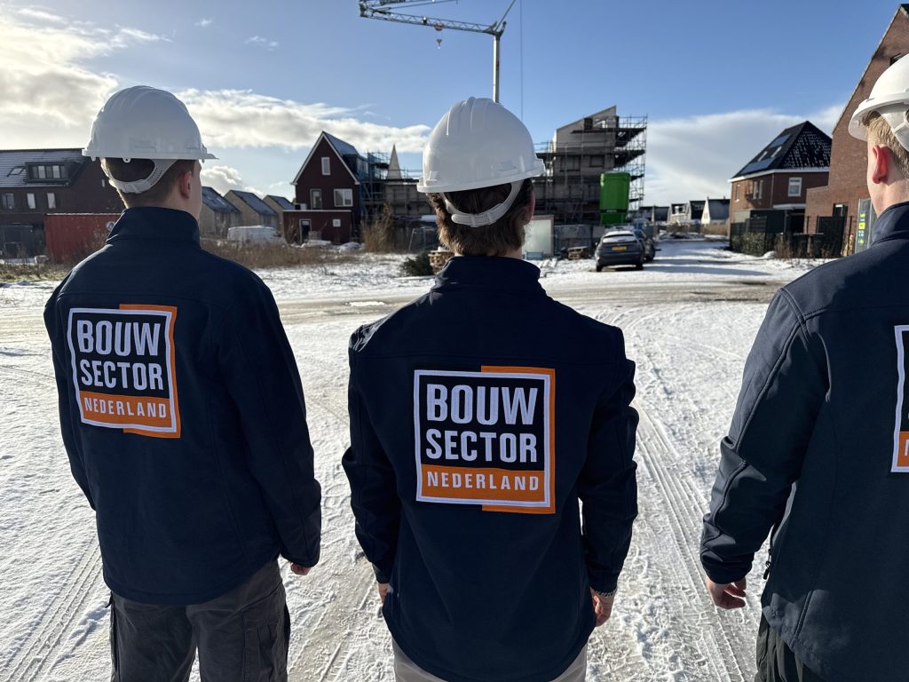 Drie vakmensen van Bouwsector Nederland met witte helm en logo op de rug bij woningen in aanbouw